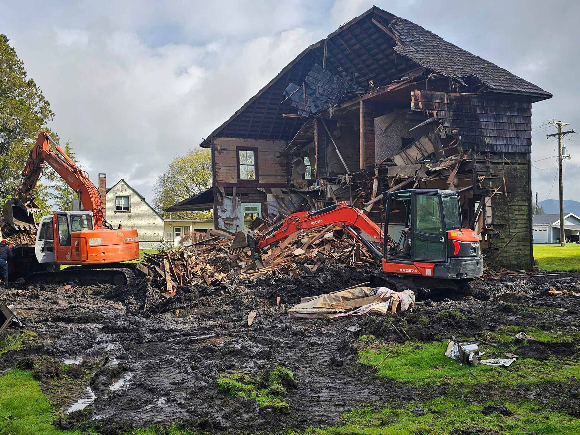 Workers from Salish Excavation and Trucking LLC demolishing an dilapidated house with orange excavators