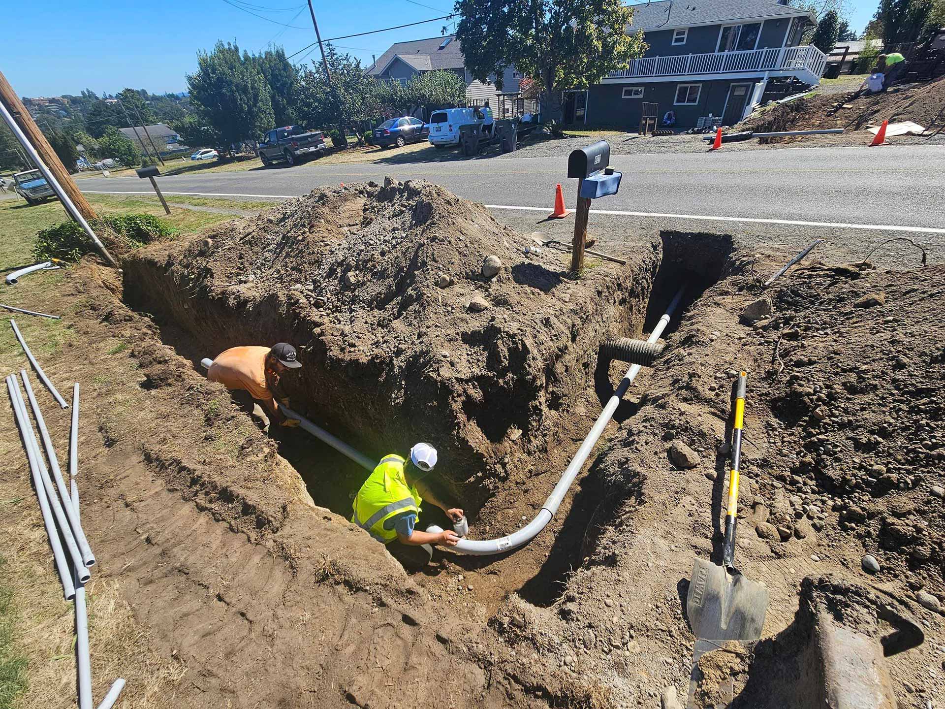 Workers from Salish Excavation and Trucking LLC installing utility line in trench